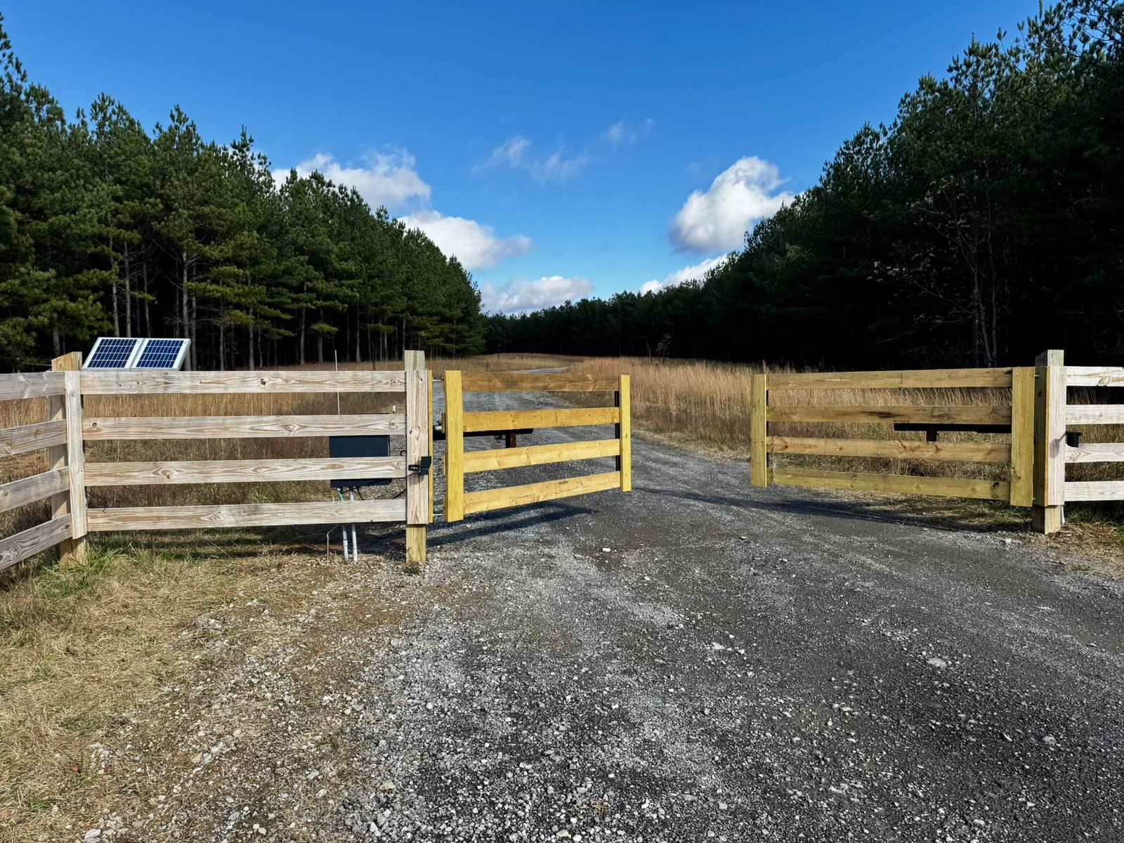 Solar-powered wooden ranch gate on a gravel drive through North Georgia pines