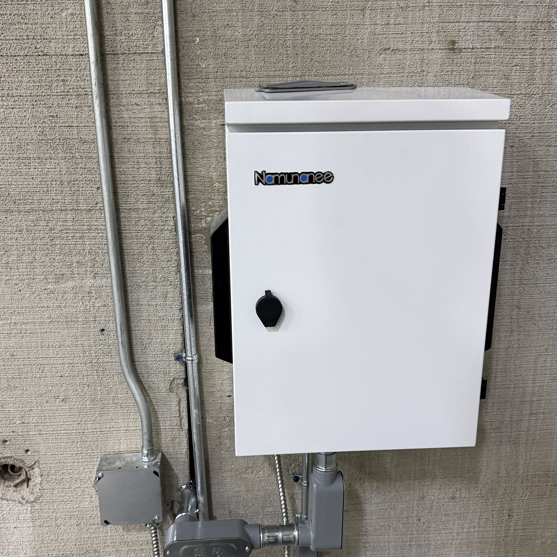 Wall-mounted equipment enclosure with neat metal conduit runs on a concrete wall