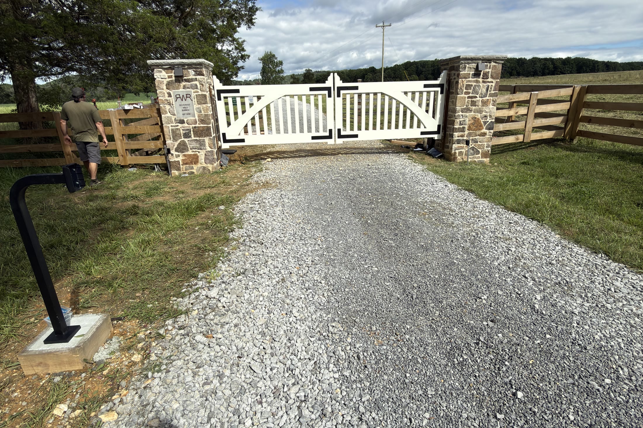 White estate driveway gate between stone pillars with a gooseneck access pedestal in the foreground